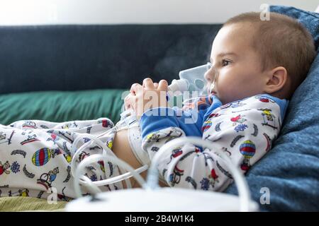 Ragazzo che tiene la maschera nasale mentre fa l'inalazione con nebulizzatore Foto Stock