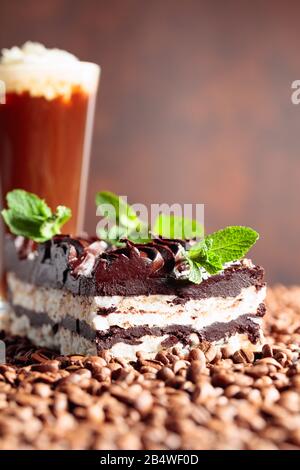 Deliziosa torta al cioccolato con menta e bevanda al caffè con panna. I chicchi di caffè sono sparsi sul tavolo. Foto Stock