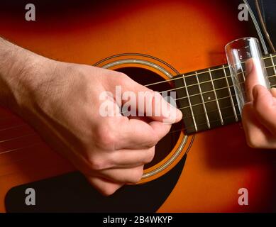 Uomo che suona una chitarra acustica con uno scivolo di vetro. Foto Stock