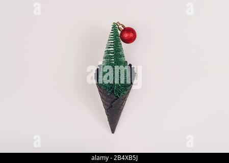 Mini albero di natale con palla rossa in nero ghiaccio-corno su sfondo pastello con spazio copia. Immagine creativa e moody. Confetto di Natale. Foto Stock