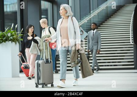 Full shot orizzontale di donna moderna senior che cammina lungo la sala dell'aeroporto con i suoi bagagli, copia spazi Foto Stock