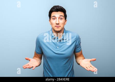 bell'uomo brunetta in polo blu con faccia seria gesturante con le mani su uno sfondo blu. studio sparare. non c'è niente da fare Foto Stock