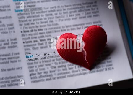 Cuore rotto rosso sulla definizione dell'amore del dizionario. Il concetto di cuore spezzato, divisione, infedeltà . Messa a fuoco selettiva. Foto Stock