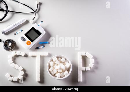 Stile di vita sano, concetto di cibo e sport. Vista dall'alto del set di tester per il diabete e dello stetoscopio con cubetti, segno DI STOP dello zucchero su sfondo grigio scuro. Foto Stock