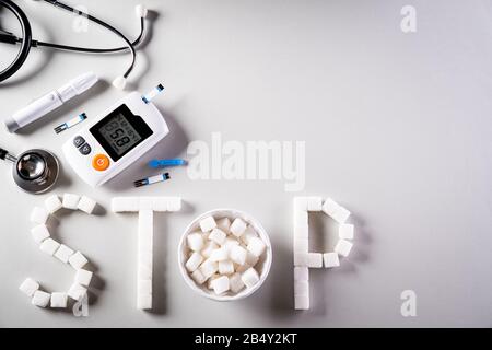 Stile di vita sano, concetto di cibo e sport. Vista dall'alto del set di tester per il diabete e dello stetoscopio con cubetti, segno DI STOP dello zucchero su sfondo grigio scuro. Foto Stock