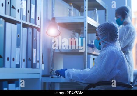 Proiezione orizzontale laterale di due scienziati medici non riconoscibili in tute protettive che lavorano in un moderno laboratorio Foto Stock