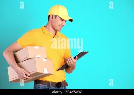 Uomo di consegna felice in polo giallo uniforme casella postale pacco e lista di controllo isolato su sfondo verde brillante pastello. Sorridente Courier De Foto Stock