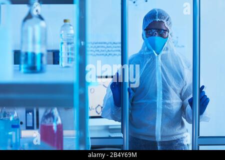 Medico maschile irriconoscibile in indumenti da lavoro protettivi aprire porte e entrare in sala da laboratorio, foto orizzontale, copia spazio Foto Stock