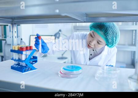 Dose di primo piano orizzontale media di giovane lavoratore di laboratorio asiatico che esegue la provetta con il campione Foto Stock