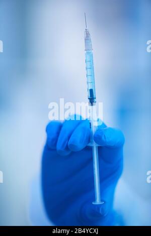 Mano della donna in una siringa blu usa e getta in lattice per il mantenimento del glive piena di nuovo vaccino, colpo ravvicinato verticale Foto Stock
