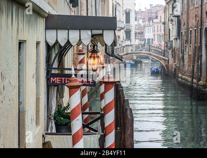 Guardando su un canale veneziano con un ingresso di taxi d'acqua dell'hotel e un ponte ornato sullo sfondo, Venezia, Italia in una fredda e nebbiosa mattina d'inverno Foto Stock
