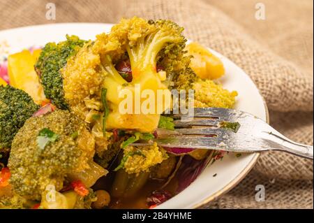 Insalata di verdure in una ciotola bianca di ceramica e forchetta su uno sfondo di tessuto di homespun grezzo. Primo piano Foto Stock