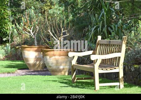 Una panca in legno accanto a due urne in terracotta a Rosemoor, un giardino di campagna inglese, nel Devon del Nord, Inghilterra. Foto Stock