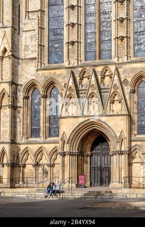 Un'immagine ravvicinata della famosa cattedrale medievale di York con ombre che cadono sulla sua architettura gotica. Una giovane coppia si siede sui gradini. Foto Stock