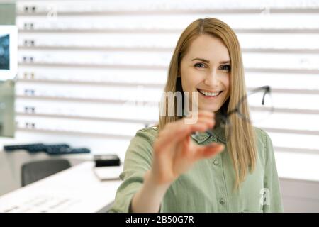 giovane donna sorridente che sceglie nuovi occhiali in negozio di ottica Foto Stock
