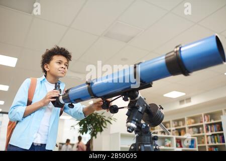 Orizzontale medio basso angolo shot di afroamericano scuola media utilizzando moderno telescopio a qualcosa di lontano, copia spazio Foto Stock
