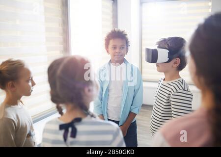Studenti della scuola media che testano occhiali VR, i suoi compagni di classe che si stanno intorno a lui aspettando il loro turno Foto Stock