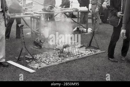 Anni '1970, storico, grandi pezzi di carne cucinati su un barbecue fai da te, una griglia metallica sopra un fuoco aperto sedeva sull'erba ad un evento all'aperto, Inghilterra, Regno Unito. Foto Stock