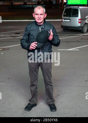 Un uomo con un berretto da baseball nelle sue mani di notte sulla strada. Immagine sfondo persone. Giorno del Padre. Inserire il testo. Capelli grigi. Foto Stock