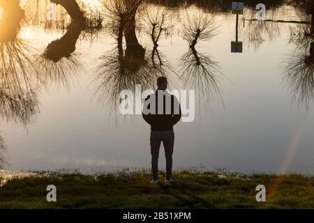 Un giovane osserva l'inondazione del fiume Cherwell che rende un pub giardino a Oxford inaccessibile dopo la pioggia intensa Foto Stock