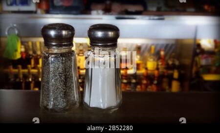 Shaker di sale e pepe su un bar in una taverna locale con bottiglie di liquore sfocate sullo sfondo Foto Stock