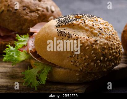 Delizioso hamburger croccante con prosciutto affettato su un tagliere di legno vintage. Foto di cibo scuro ottimo per il menu del bar e i poster. Foto Stock