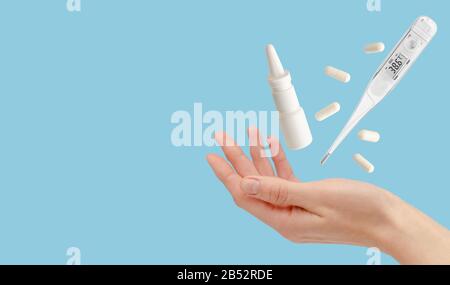 Termometro, medicina e spray nasale che volano su mano femmina isolato su blu. Concetto di assistenza sanitaria. Spazio di copia Foto Stock