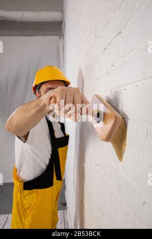 Pittore su un cantiere mentre fa il suo lavoro. È vestito con abiti da lavoro speciali. Foto Stock