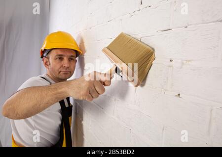 Pittore su un cantiere mentre fa il suo lavoro. È vestito con abiti da lavoro speciali. Foto Stock