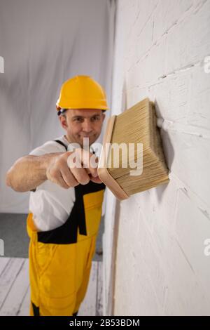 Pittore su un cantiere mentre fa il suo lavoro. È vestito con abiti da lavoro speciali. Foto Stock