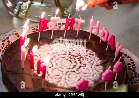 Burning felice lettera di compleanno candele sulla torta di cioccolato decorato con zucchero rangoli primo piano Foto Stock