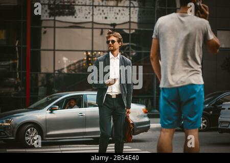 Uomo d'affari che attraversa la strada con lo smartphone in mano Foto Stock