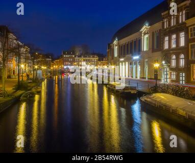Leiden, Olanda, Paesi Bassi, 16 Gennaio 2020. La vista notturna delle biciclette parcheggiate tutto intorno, ponti, strade, canali, caffè, chiatte nella città vecchia, barca Foto Stock