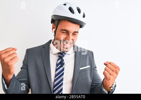 Giovane bel casco da uomo d'affari bici e cuffie wireless su sfondo isolato molto felice ed eccitato facendo il gesto del vincitore con le braccia sollevate, Foto Stock