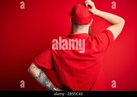 Giovane e bello consegna uomo indossando occhiali e tappo rosso su sfondo isolato Indietro pensando al dubbio con la mano sulla testa Foto Stock