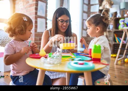 Giovane bella insegnante e i bimbi a giocare i pasti utilizzando plastica alimentare e posate giocattolo al kindergarten Foto Stock