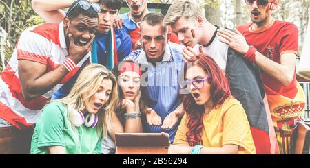 Tifosi felici di diversi paesi che guardano lo sport di calcio su tablet computer blocco note - Focus principale sui ragazzi del centro - Multirazzial tifosi sono shockke Foto Stock