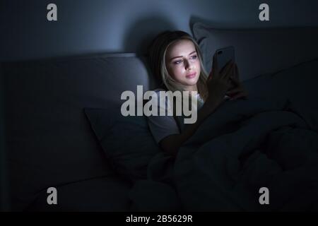 Dipendenza, nomofobia, insonnia, concetto di disturbo del sonno. Donna addicted allo smartphone connesso 24 ore su 24, 7 giorni su 7 a Internet, sdraiato a letto e utilizzando smart pho Foto Stock