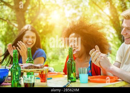 Amici felici che hanno barbecue pasto all'aperto con luce del sole posteriore - giovani che hanno a barbecue festa tostare birre - amicizia, estate e cena concep Foto Stock