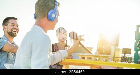 Giovani felici che fanno un video live streaming da Beach party al tramonto - Man vlogger registrazione video feed sulla spiaggia al tramonto - Focus sulla sinistra Foto Stock