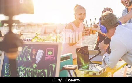 Gruppo di giovani che si rallegrano con i cocktail mentre fanno un video live streaming da Beach party al tramonto - nuovo trend tecnologico, stile di vita giovanile, Foto Stock