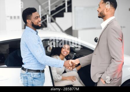 Il Venditore Di Automobili Scuotendo Le Mani Con Gli Acquirenti Dopo Che L'Affare Riuscito All'Interno Foto Stock