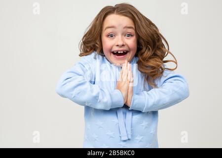 cute ragazza adolescente in una felpa con cappuccio blu prega di acquistare qualcosa su uno sfondo grigio chiaro Foto Stock