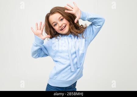 affascinante ragazza teen in una felpa con cappuccio blu mostra dieci dita su uno sfondo grigio chiaro Foto Stock