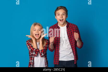 Fratelletto E Sorella Che Rallegrano Con Le Mani Alzate Su Sfondo Blu Foto Stock