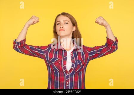 Sono donna forte! Ritratto di una ragazza di zenzero sicura di sé in camicia casual che alza le mani mostrando potenza e forza, sensazione di successo indipendente, fem Foto Stock