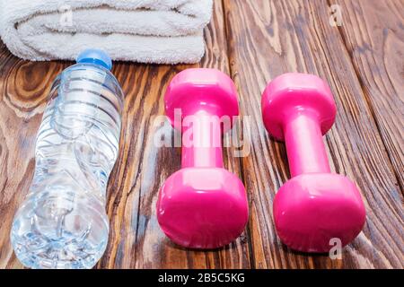 dumbbells e una bottiglia d'acqua con asciugamano su sfondo di legno, concetto di preparazione per il fitness attrezzature sportive vista dall'alto Foto Stock