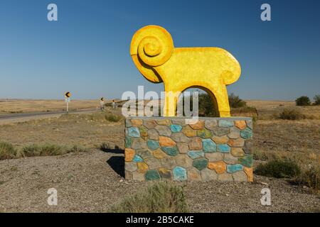 Distretto di Khromtau, Kazakhstan - 23 agosto 2019: Una statua del montone vicino alla strada. Un cartello stradale che accoglie i visitatori del quartiere Khromtau. Foto Stock