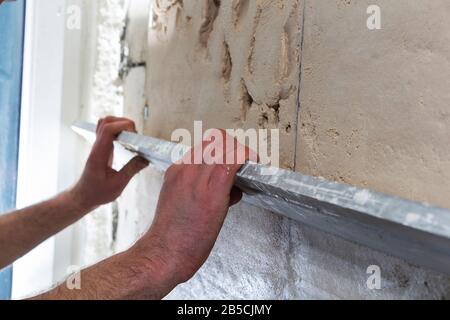 Operaio edile con una spatola lunga per intonacare il muro a mano Foto Stock