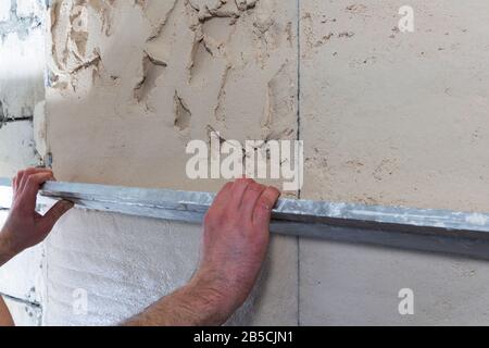 Operaio edile con una spatola lunga per intonacare il muro a mano Foto Stock